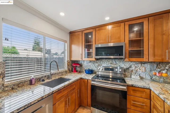 Kitchen with appliances with stainless steel finishes, light stone counters, brown cabinetry, tasteful backsplash, and ornamental molding