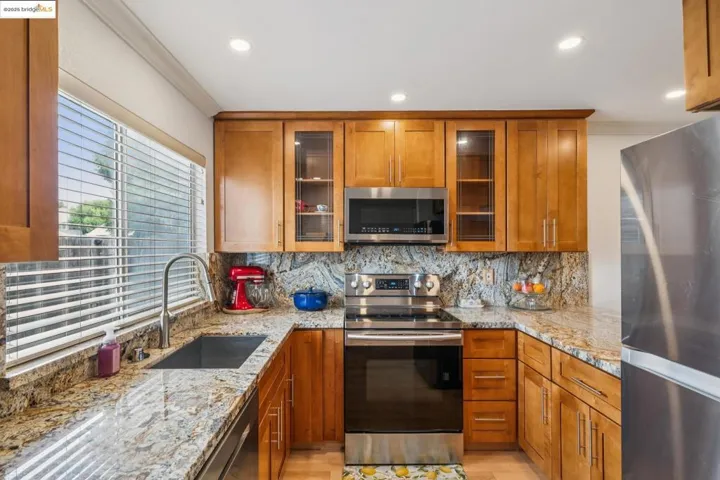 Kitchen with appliances with stainless steel finishes, brown cabinets, tasteful backsplash, light stone countertops, and crown molding