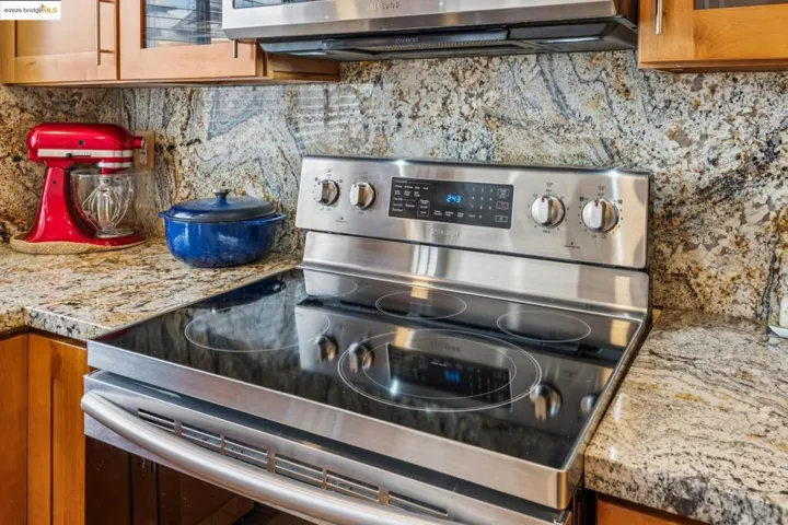 Kitchen view of light stone countertops, brown cabinets, stainless steel appliances, and tasteful backsplash
