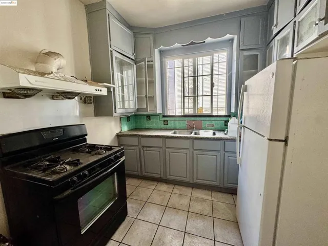 Kitchen featuring gray cabinetry, black gas range, freestanding refrigerator, light tile patterned flooring, and light countertops