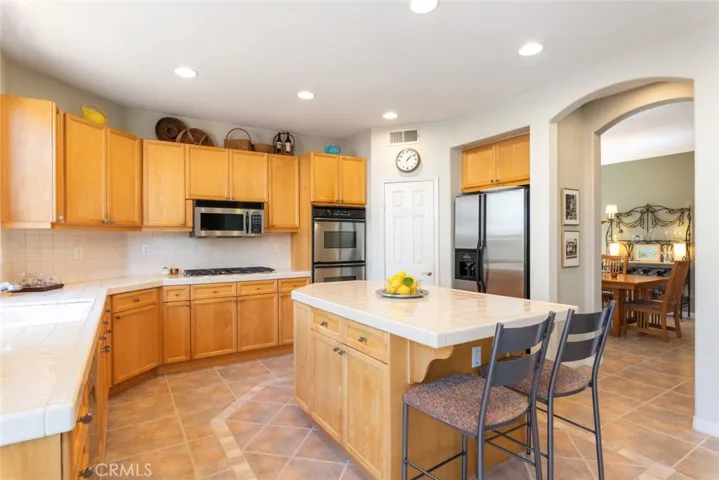 chef’s kitchen with large island and seating, built-in gas cooktop, double wall oven, and stainless steel refrigerator.