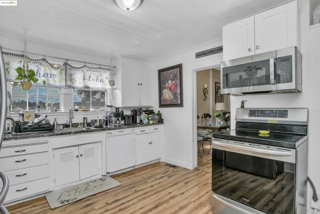 Kitchen with appliances with stainless steel finishes, white cabinets, light wood-style flooring, and dark stone countertops