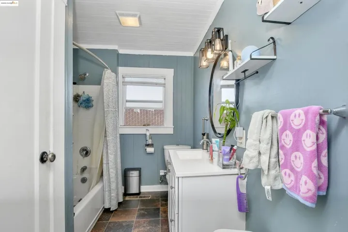 Full bathroom with shower / bath combo, vanity, dark stone finish flooring, and wooden walls