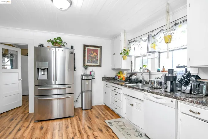 Kitchen featuring white cabinets, stainless steel fridge with ice dispenser, dishwasher, light wood-style floors, and dark stone counters