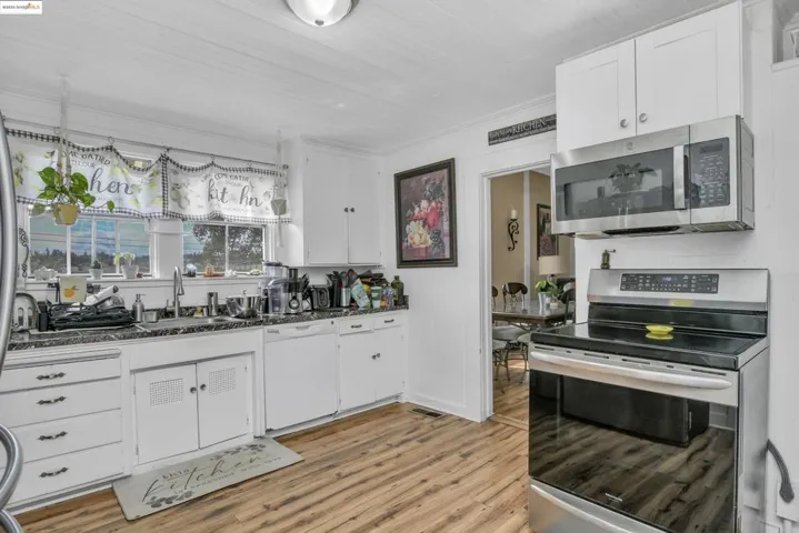 Kitchen with appliances with stainless steel finishes, white cabinets, light wood-style flooring, and dark stone countertops