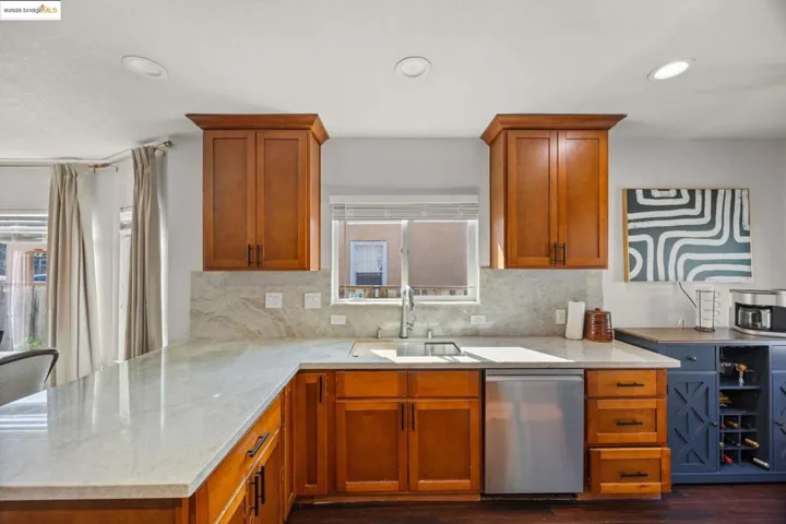 Kitchen featuring brown cabinetry, light stone counters, stainless steel dishwasher, and recessed lighting