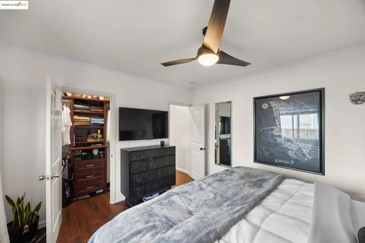 Bedroom featuring dark wood-type flooring, ornamental molding, a ceiling fan, and a walk in closet