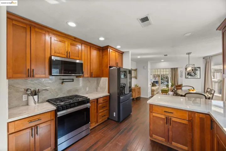 Kitchen featuring brown cabinetry, light stone countertops, stainless steel appliances, tasteful backsplash, and pendant lighting