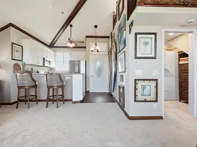 Balcony view frames the leaded-glass front door, while the sunlit living space reveals new carpeting, loft above, kitchen bar seating, walk-in closet, and multiple ceiling fans throughout.