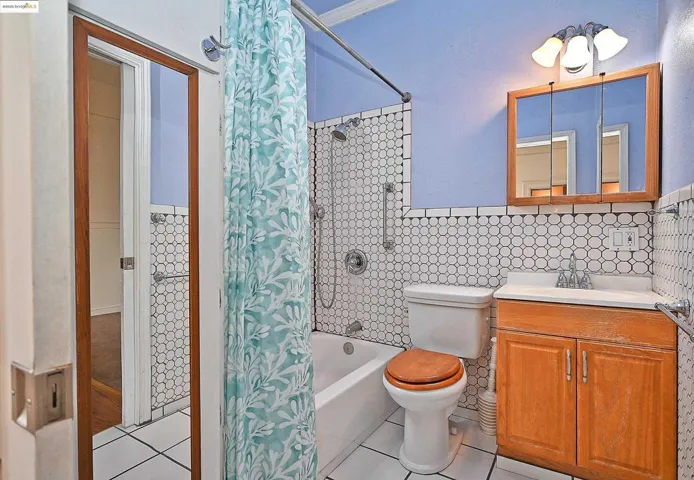 Full bath featuring shower / bath combo with shower curtain, vanity, tile patterned floors, and tile walls