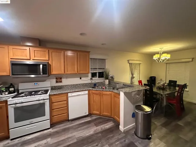 Kitchen featuring white appliances, a peninsula, dark stone counters, dark wood-style flooring, and recessed lighting