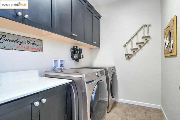 Washroom with cabinet space, separate washer and dryer, light tile patterned floors, and a textured wall