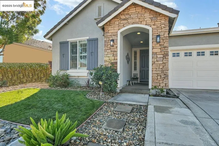 Property entrance featuring stone siding, stucco siding, a lawn, an attached garage, and concrete driveway