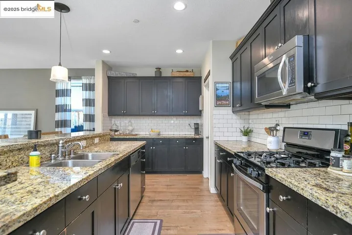 Kitchen with stainless steel appliances, light stone countertops, decorative light fixtures, light wood-style flooring, and backsplash