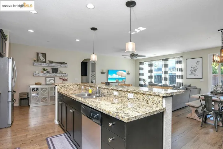 Kitchen featuring hanging light fixtures, appliances with stainless steel finishes, open floor plan, ceiling fan, and dark cabinetry