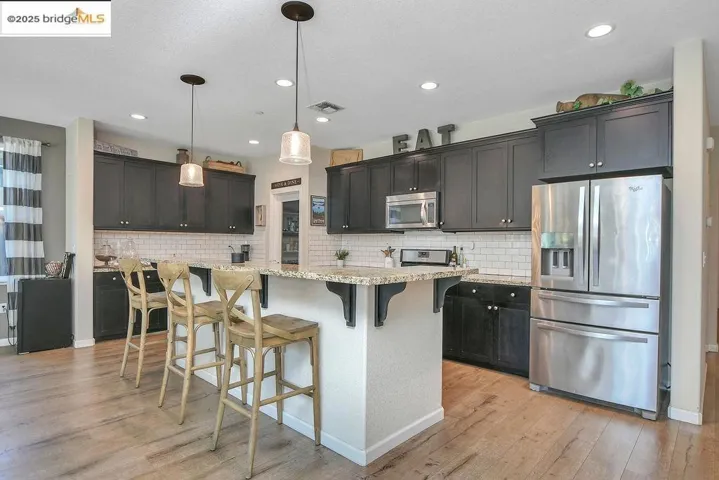 Kitchen featuring stainless steel appliances, a kitchen breakfast bar, hanging light fixtures, light stone counters, and backsplash