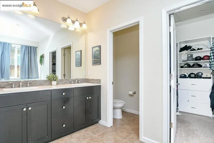 Full bathroom with a walk in closet, double vanity, and light tile patterned flooring