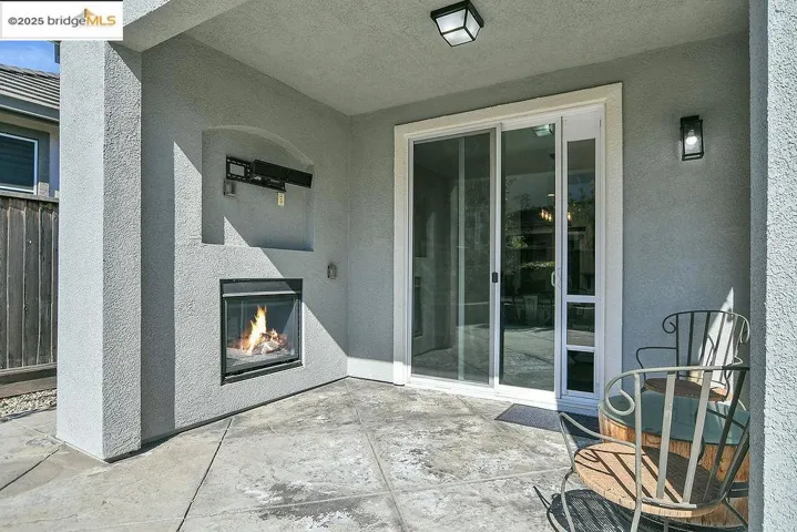 Entrance to property featuring a glass covered fireplace, a patio, and stucco siding