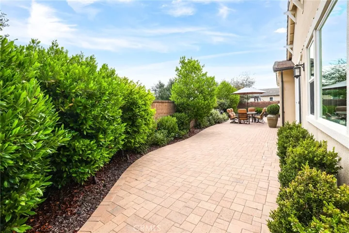 Outdoor walkway framed by dense greenery, leading to the backyard.