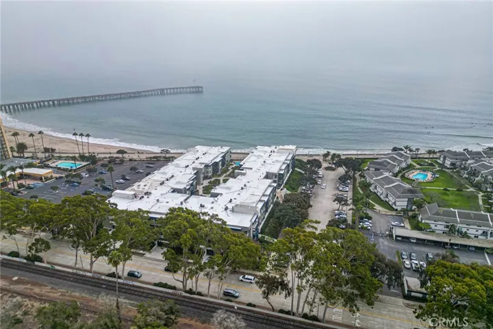The building with white rooftops is the complex. The unit is on the right side. Parking is available on the right side. The pier is in the near distance. Train tracks in the foreground.