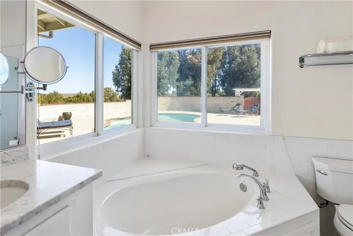 Soaking tub framed by corner windows with views of the pool, vineyard, and hills.