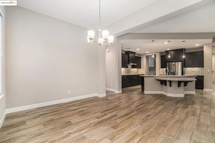 Kitchen with a breakfast bar area, a center island with sink, stainless steel refrigerator with ice dispenser, a chandelier, and decorative light fixtures