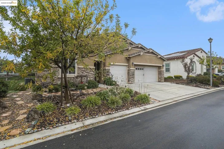 View of front of house with stucco siding, stone siding, driveway, and an attached garage