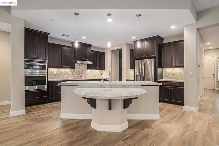 Kitchen with dark brown cabinets, hanging light fixtures, appliances with stainless steel finishes, a kitchen island with sink, and recessed lighting
