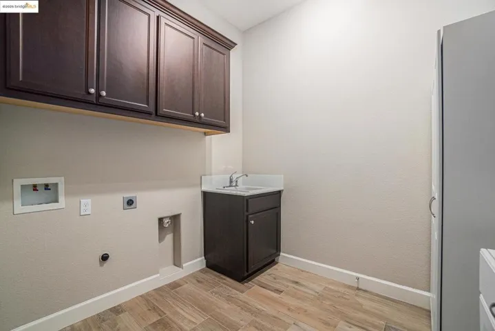 Laundry area featuring light wood-type flooring, hookup for an electric dryer, cabinet space, hookup for a washing machine, and a textured wall