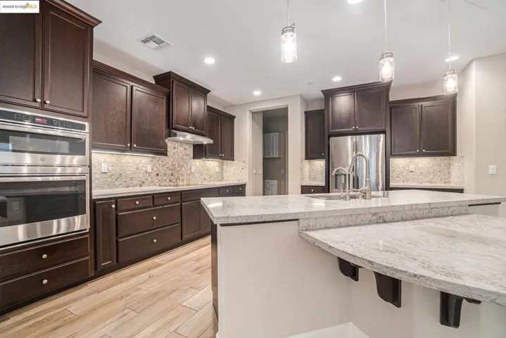 Kitchen featuring dark brown cabinetry, appliances with stainless steel finishes, decorative light fixtures, a large island, and recessed lighting