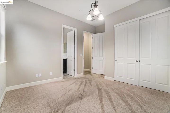 Unfurnished bedroom featuring a chandelier, light carpet, ensuite bath, and a closet