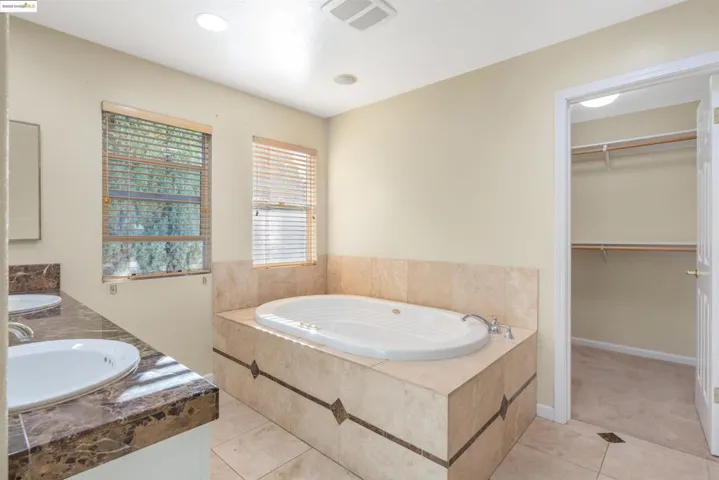 Bathroom with double vanity, a bath, light tile patterned floors, a walk in closet, and recessed lighting
