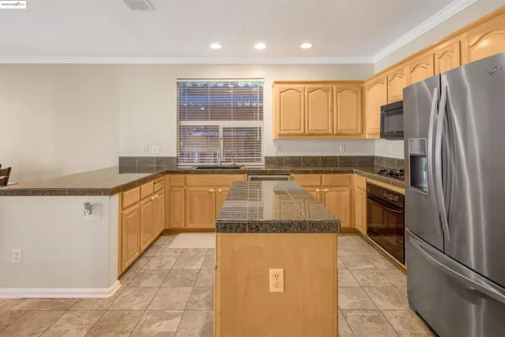 Kitchen with tile countertops, black appliances, a peninsula, light brown cabinets, and recessed lighting