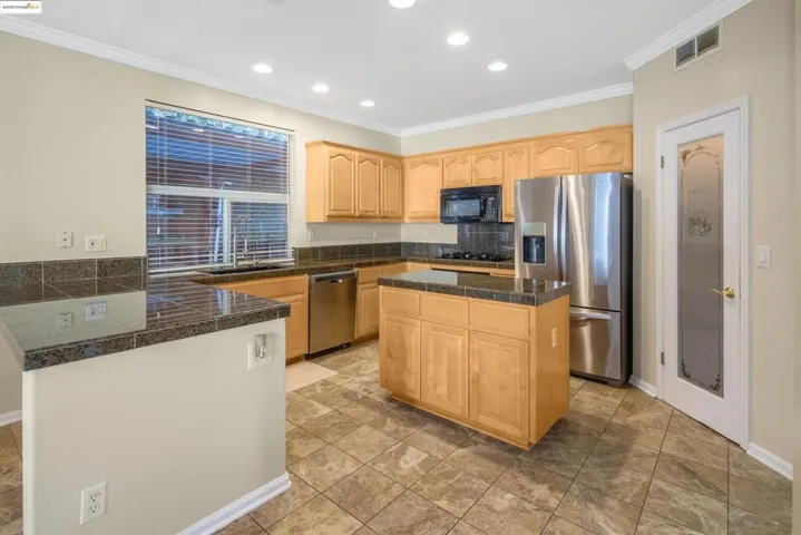Kitchen featuring tile counters, decorative backsplash, appliances with stainless steel finishes, light brown cabinetry, and a peninsula