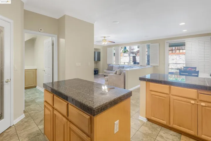 Kitchen with tile countertops, a kitchen island, ceiling fan, ornamental molding, and open floor plan