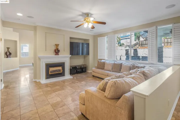 Living room featuring crown molding, plenty of natural light, a glass covered fireplace, and a ceiling fan