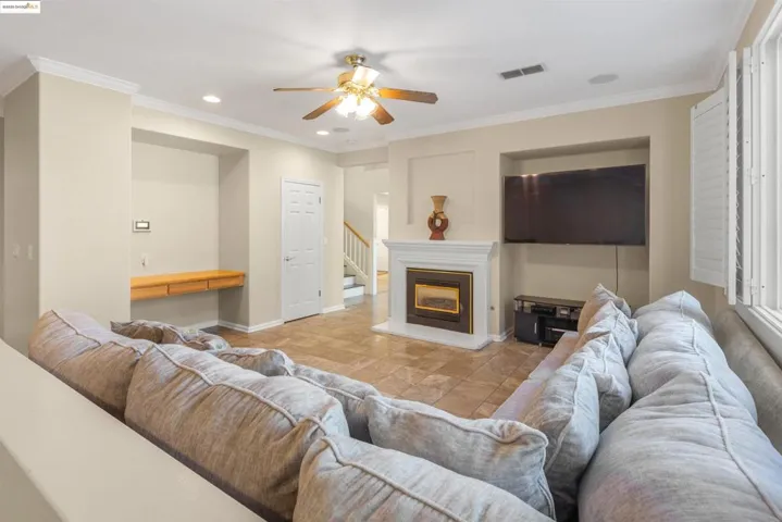 Living room with built in study area, recessed lighting, ornamental molding, a glass covered fireplace, and stairway