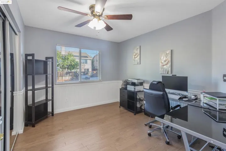 Home office with light wood-style floors, a wainscoted wall, and ceiling fan