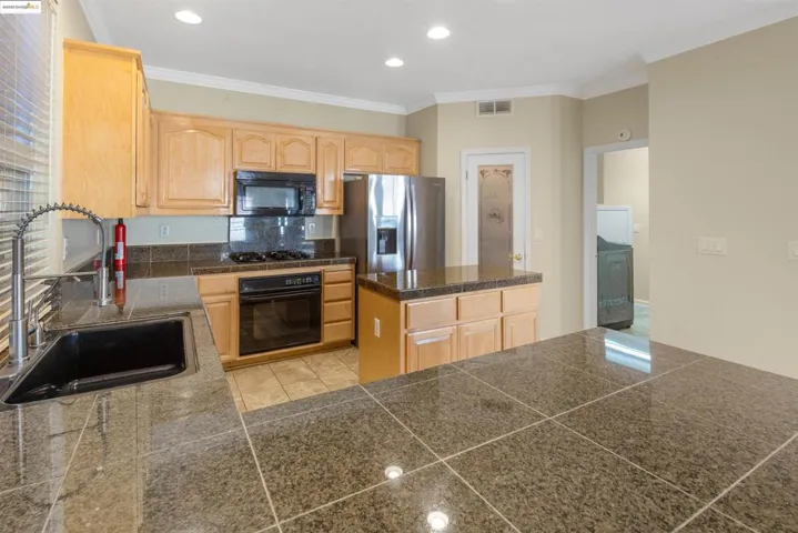 Kitchen with tile counters, light brown cabinets, black appliances, ornamental molding, and recessed lighting
