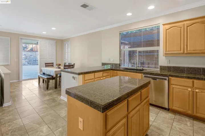 Kitchen with tile counters, a peninsula, crown molding, stainless steel dishwasher, and recessed lighting