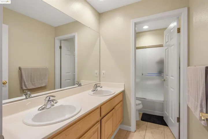 Full bath featuring double vanity, light tile patterned floors, and enclosed tub / shower combo