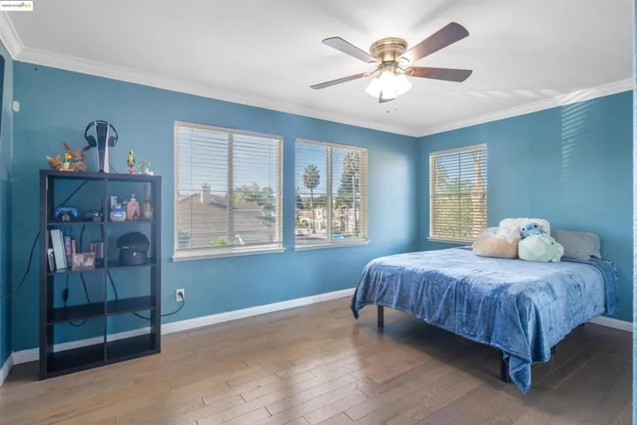 Bedroom featuring crown molding, multiple windows, hardwood / wood-style flooring, and a ceiling fan