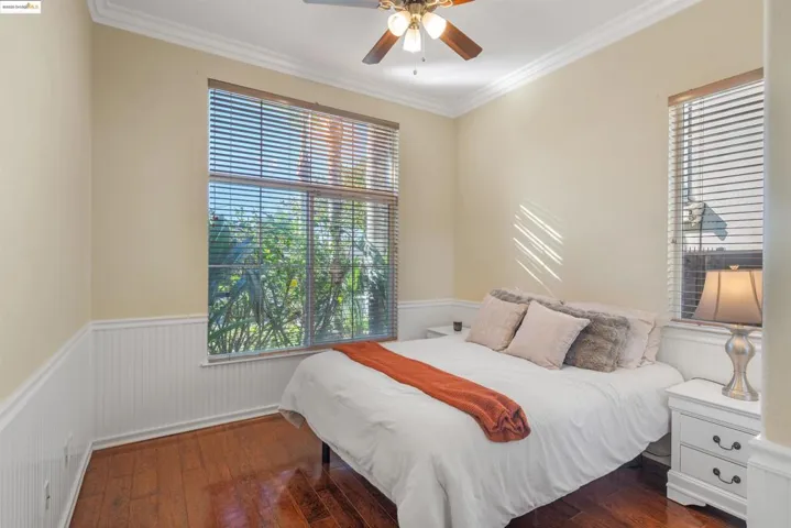 Bedroom with crown molding, dark wood-type flooring, wainscoting, multiple windows, and a ceiling fan