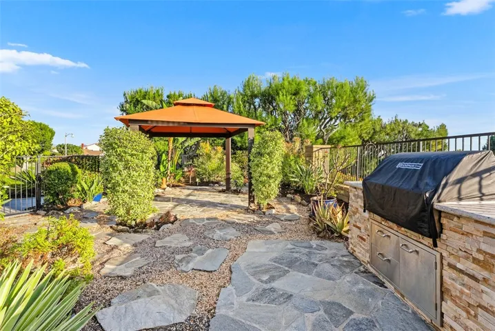 Outdoor kitchen including a built-in BBQ island and beverage fridge and a gazebo tucked within the beautifully landscaped side garden