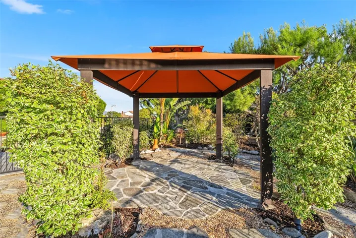 Outdoor kitchen including a built-in BBQ island and beverage fridge and a gazebo tucked within the beautifully landscaped side garden