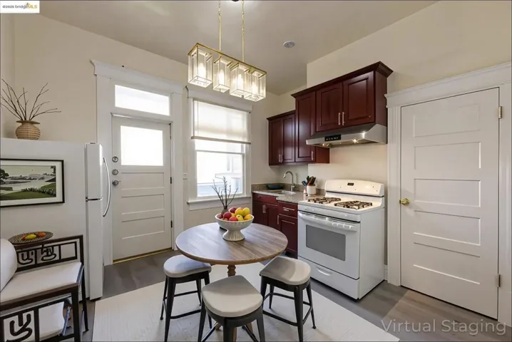 Virtually staged Kitchen featuring white gas range, dark wood-type flooring, under cabinet cabinet range hood and kitchen sink, and pantry.