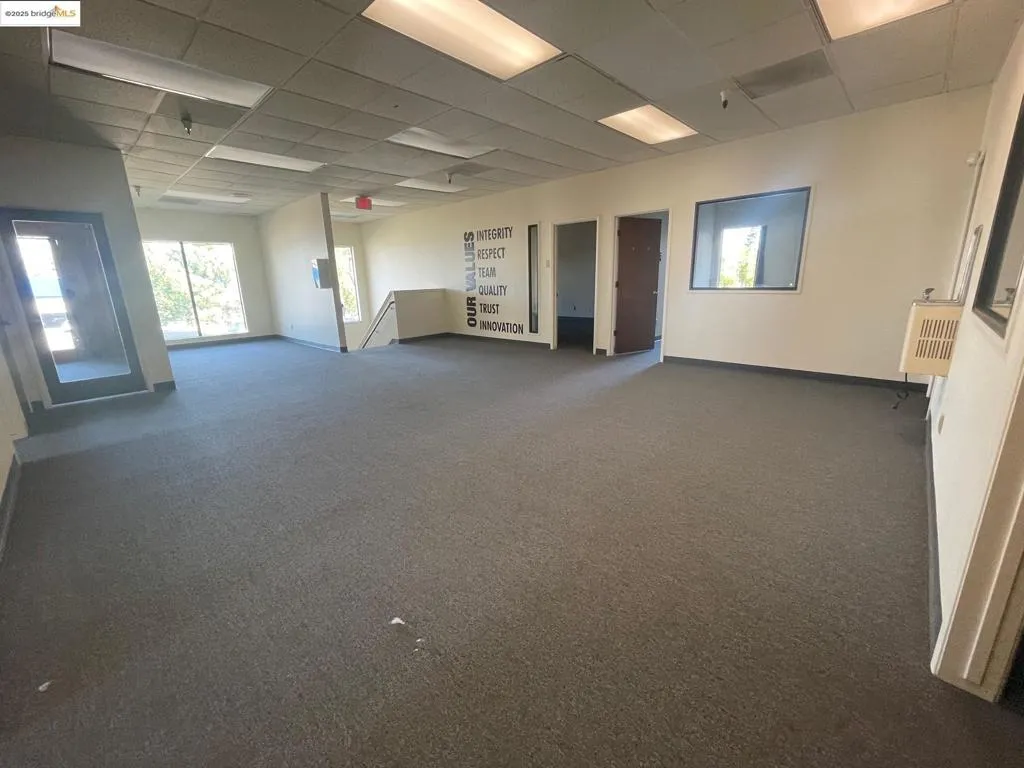Empty room featuring a paneled ceiling, dark colored carpet, and heating unit