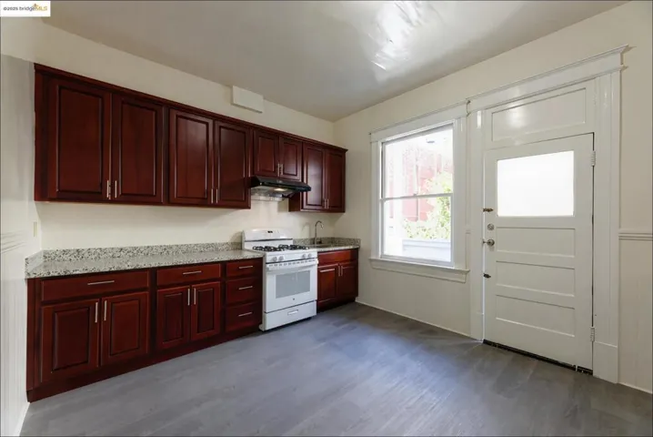 Empty Kitchen featuring white gas range oven, dark wood finished floors, light stone counters, under cabinet range hood, and reddish brown cabinets