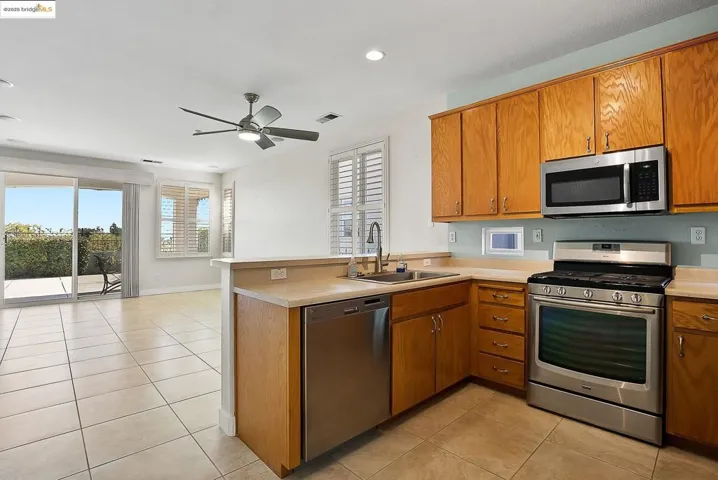 Kitchen with appliances with stainless steel finishes, a peninsula, light countertops, brown cabinetry, and light tile patterned floors