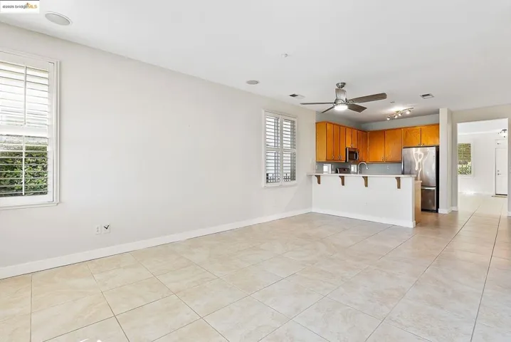 Kitchen with a breakfast bar, brown cabinetry, light countertops, stainless steel appliances, and light tile patterned floors